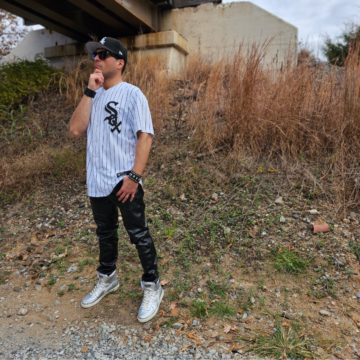 Cosmicus in Chicago White Sox Jersey and faux leather punk pants and shiny diadora high top sneakers by railroad tracks in city thinking and pondering