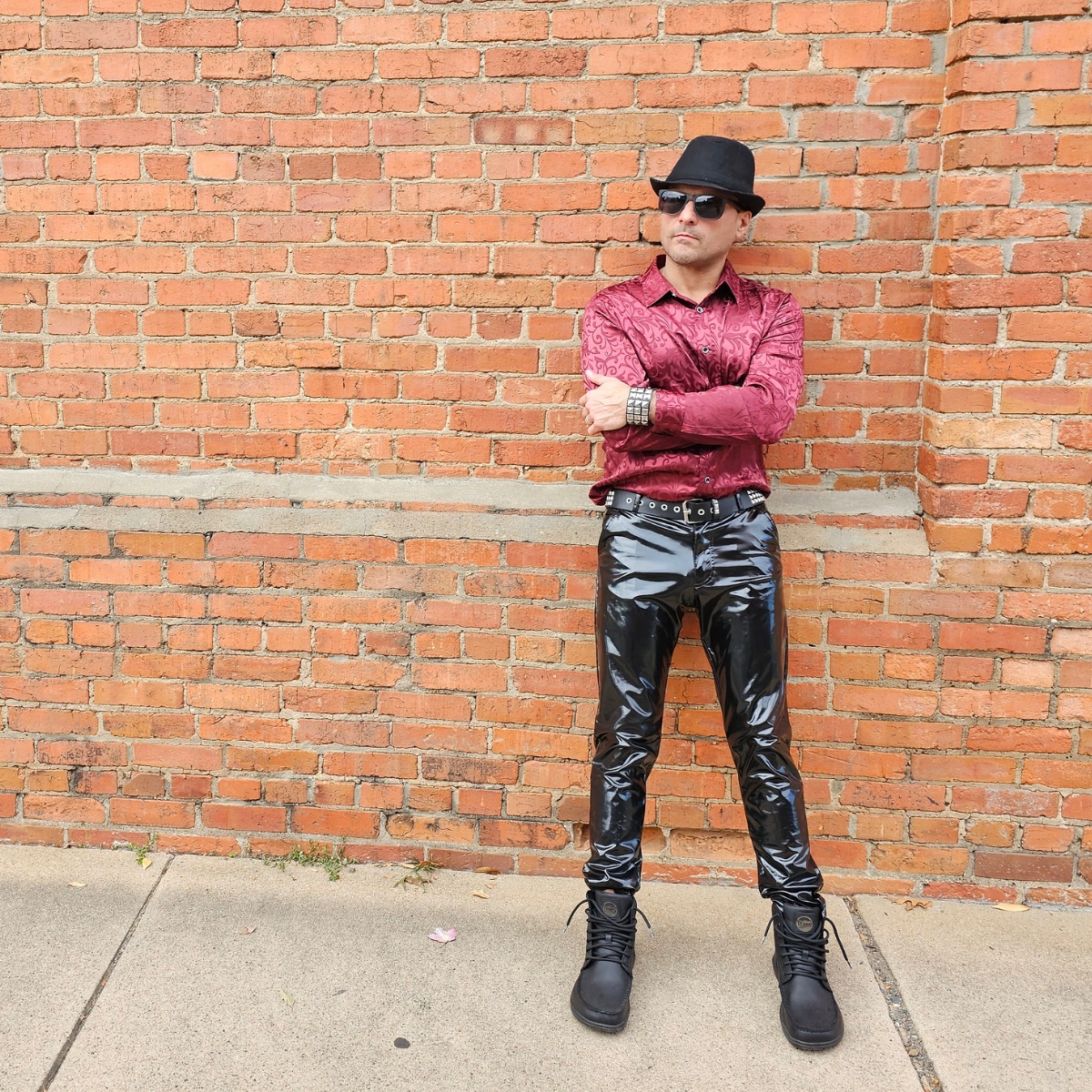 Cosmicus in city standing on brick wall in shiny faux leather pvc pants and boots 2